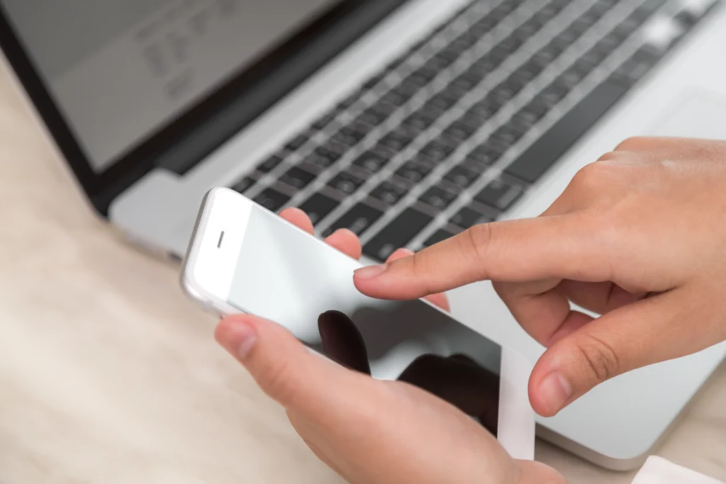 persona tocando un telefono con un portatil de fondo